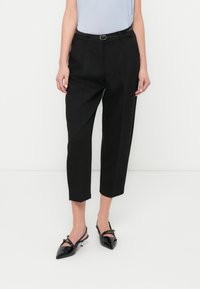 Μαύροι κομμένοι παντελόνια με ραμμένη εφαρμογή, που διαθέτουν θηλιές για ζώνη και μέση με ζώνη, συνδυασμένα με γυαλιστερά μαύρα παπούτσια μυτερά στο μπροστινό μέρος.