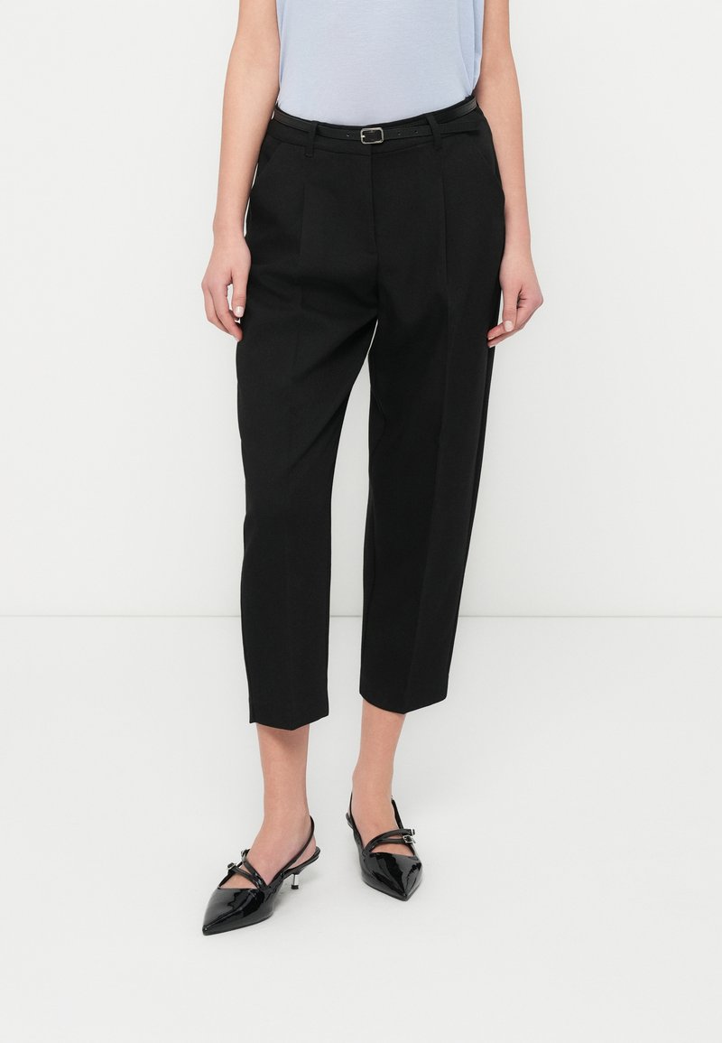 Μαύροι κομμένοι παντελόνια με ραμμένη εφαρμογή, που διαθέτουν θηλιές για ζώνη και μέση με ζώνη, συνδυασμένα με γυαλιστερά μαύρα παπούτσια μυτερά στο μπροστινό μέρος.