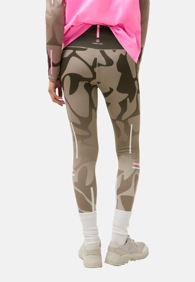 Dopasowane legginsy w kamuflażu w odcieniach beżu i brązu z białymi i różowymi paskami, wykonane z elastycznego materiału, zestawione z białymi skarpetkami i butami.