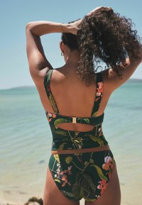 Zeleni cvjetni bikini top s širokim naramenicama i izrezom na leđima, u kombinaciji s odgovarajućim donjim dijelom. Sadrži tropske uzorke na glatkom materijalu.
