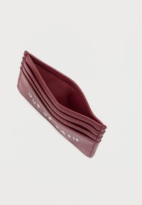 Kaarthouder van bordeauxrood leer met meerdere vakken, voorzien van een gestructureerde afwerking en de tekst "OUT OF CASH" in het wit gedrukt.