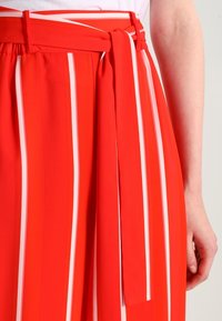 Rode wijde broek met witte verticale strepen, voorzien van een ceintuur in de taille en een gladde, licht glanzende textuur.