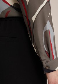 Bluză cu mâneci lungi, cu un model abstract multicolor în nuanțe de gri, roșu și albastru, asociată cu un brâu negru și manșete cu nasturi.