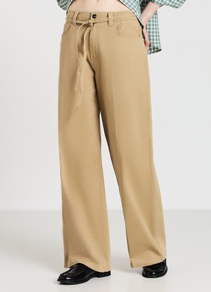 Pantaloni beige a gamba larga con vita con coulisse, tasche laterali e texture liscia, abbinati a mocassini neri.