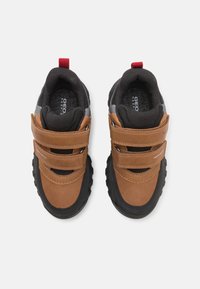Scarpe in suede marrone e mesh nero con due fasce in Velcro, suole in gomma nera e un tassello rosso sul tallone. Dettagli logo sottili presenti.