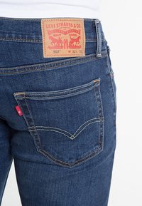 Mörkblå denim Levi's 502-jeans med en röd flik, som har en brun läderlapp på midjan och karakteristisk bakfickssöm.