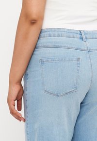 Calças de ganga de denim azul claro com uma textura suave, apresentando um único bolso traseiro e um design de corte reto. A cinta é ligeiramente curva.