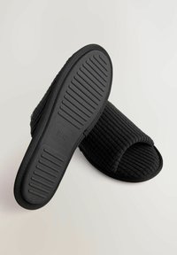 Chaussons en tissu noir avec une texture nervurée, une conception à bout ouvert et une semelle en caoutchouc flexible. L'étiquette de taille 8/42 est visible sur la semelle.