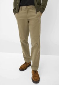 Chinos beige con vestibilità slim, dotati di chiusura con bottone e tasca con zip. Abbinati a scarpe marroni in suede con lacci.