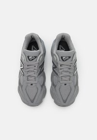 Des chaussures de sport grises en matériau mesh et synthétique, avec des accents noirs, un design à lacets et une semelle rembourrée.