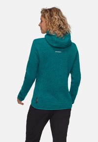 Felpa in pile teal con un motivo testurizzato, cappuccio attaccato e logo sul retro. Maniche lunghe e orlo leggermente curvato.