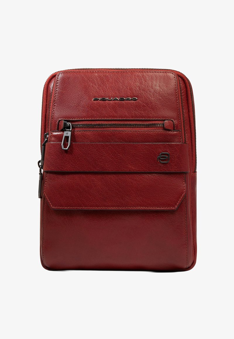 Sac rectangulaire vertical en cuir rouge avec deux compartiments zippés, une poche avant à rabat et des accents de logo de marque en métal.