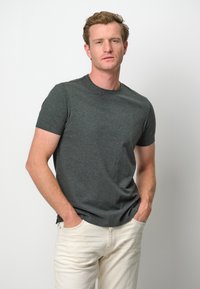 Mörkgrå, kortärmad t-shirt tillverkad av mjuk bomullsblandning, med rund halsringning och avslappnad passform, kombinerad med ljusa byxor.