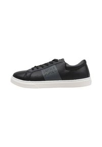 Zapatilla de cuero negra con suela de goma blanca, que presenta un diseño de raya texturizada en el costado y cordones negros. Forma simple y moderna.