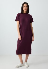 Burgundowa sukienka t-shirtowa z krótkimi rękawami, długość do kolan, miękka tkanina, gładka faktura, zestawiona z białymi sneakersami.
