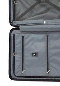 Intérieur d'une valise grise ouverte montrant un compartiment en maille avec fermeture éclair et un diviseur en tissu avec trois fermetures éclair verticales ainsi qu'un petit logo.