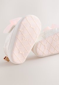 Witte sneakers met een roze, getextureerde zool met een gewatteerd patroon en versierd met een zachtroze strikdetail aan de achterkant.