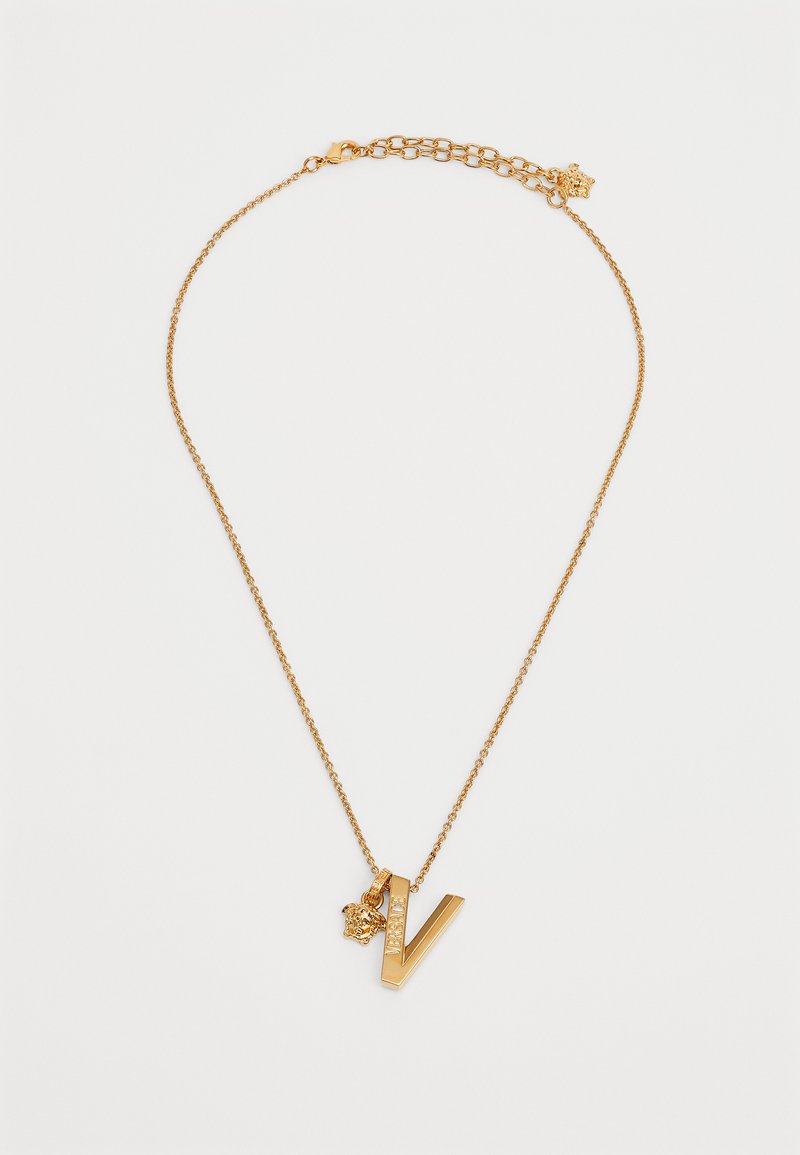 Kuldtooni kaelakee, mis omadab stiliseeritud "V" ripatsit selgete aktsentidega ja väikse amuletiga. Ahela disain on õrn ja lingitud.