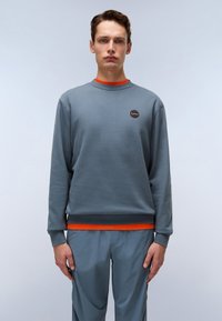 Grå hettegenser med lange ermer, ribbestrikkede mansjetter, oransje detaljer ved kragen og nederkanten, med et rundt logo på brystet.