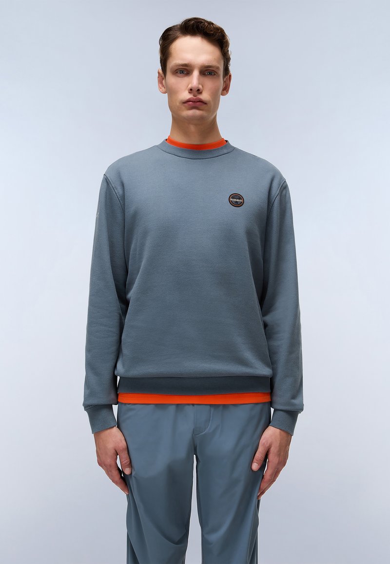 Grå hettegenser med lange ermer, ribbestrikkede mansjetter, oransje detaljer ved kragen og nederkanten, med et rundt logo på brystet.