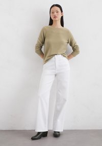 Olive green long-sleeve knit top paired with high-waisted white wide-leg jeans, worn with black block-heeled ankle boots.