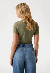 Olive green fitted t-shirt with short sleeves paired with high-waisted light blue denim jeans featuring a triangular logo on the back pocket.