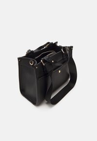 Czarna skórzana torebka z złotymi akcentami, szerokim paskiem na ramię oraz zamykanymi kieszeniami wewnętrznymi na białym tle.