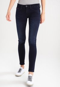 Mörkblå skinny jeans i denim med en klassisk femfickdesign och subtila sömdetaljer, bärs med vita sneakers.