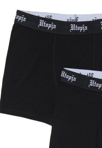 Dos bóxers negros con cinturillas negras que presentan el texto en estilo gótico blanco "Utopia".