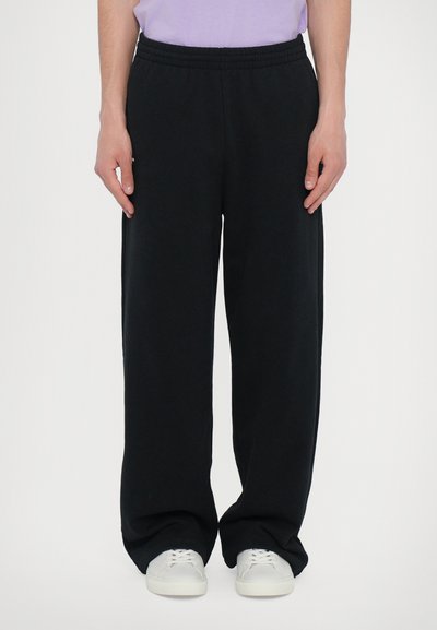 Pantalons de survêtement noirs avec une taille élastique, fabriqués en tissu doux. Coupe décontractée et jambes droites, associés à des baskets blanches.