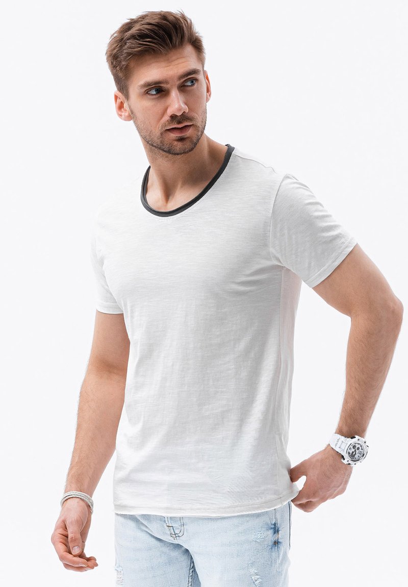 Hvid kortærmet t-shirt med en sort ribbet halskant, der har en glat tekstur og en afslappet pasform, parret med lys blå slidte jeans.