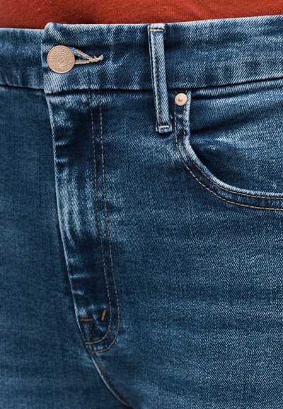 Tumed sinist värvi teksapüksid, millel on nööppandlad, taskute detailid ja nähtav õmblus. Tekstuur on sile ning kergelt kulunud välimusega.