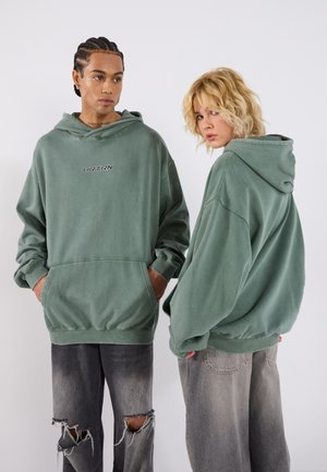 Green oversized hoodies with front pockets and embroidered "UR TRN" logo, paired with distressed black jeans. Soft fabric with a casual design.