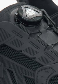 Czarny but sportowy z siateczkowym wierzchem, gumową podeszwą oraz okrągłym zapięciem do regulacji dopasowania. Tekurowane detale po bokach.