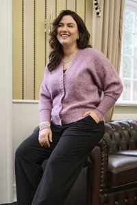 Cardigan en tricot rose doux avec un tissu texturé, présentant un col en V, une fermeture à boutons et des poignets côtelés, associé à un pantalon sombre.