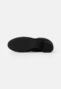 Scarpa in suede nera con suola testurizzata e tacco leggero. Presenta una finitura liscia e un marchio pronunciato sul tacco.