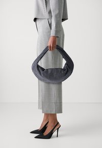 Marinblå väska med vita prickar, strukturerad form, överdimensionerat handtag, matchad med en svart och vit rutmönstrad outfit och svarta högklackade skor.
