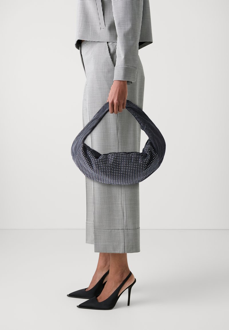 Marinblå väska med vita prickar, strukturerad form, överdimensionerat handtag, matchad med en svart och vit rutmönstrad outfit och svarta högklackade skor.