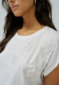 Bijela pamučna majica s tri izvezena cvijeta s detaljima od perlica na prednjoj strani, okruglim izrezom i kratkim rukavima.