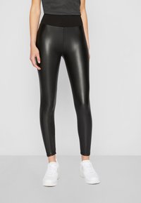 Svarta högmidjade leggings med en glänsande yta, med en mjuk midjeband och en tight passform. Bärs med vita sneakers.