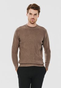 Brązowy sweter dzianinowy z okrągłym dekoltem, długimi rękawami i fakturowanym wzorem; w zestawie z ciemnymi spodniami.