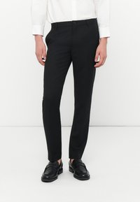 Sorte skræddersyede bukser med en slim fit, lavet af glat stof. Har en knaplukning og sidelommer, båret sammen med sorte loafers.