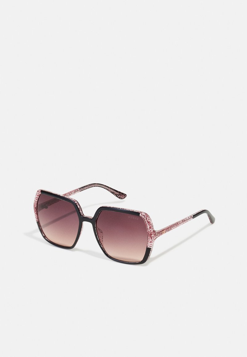 Ochelari de soare pătrați cu ramă din plastic negru, accente cu sclipici roz pe brațe și lentile colorate în gradient de la întunecat la deschis.