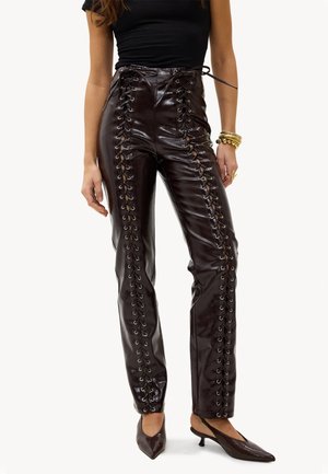 Pantalon en cuir marron foncé taille haute avec détails à lacets à l'avant, porté avec un haut noir, des bracelets dorés et des escarpins à bout pointu.