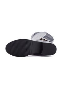 Botín gris con punta redondeada y suela plana de goma. Presenta un diseño elegante y un herraje decorativo dorado cerca del tobillo. Suela texturizada.