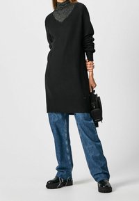 Maglione nero lungo con scollo a V, sovrapposto a un dolcevita scintillante. Abbinato a jeans di denim larghi e scarpe massicce nere.