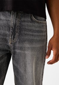 Grå denimjeans med en strukturerad finish, med gula sömmar, sidofickor och en avslappnad passform, kombinerat med en svart topp.