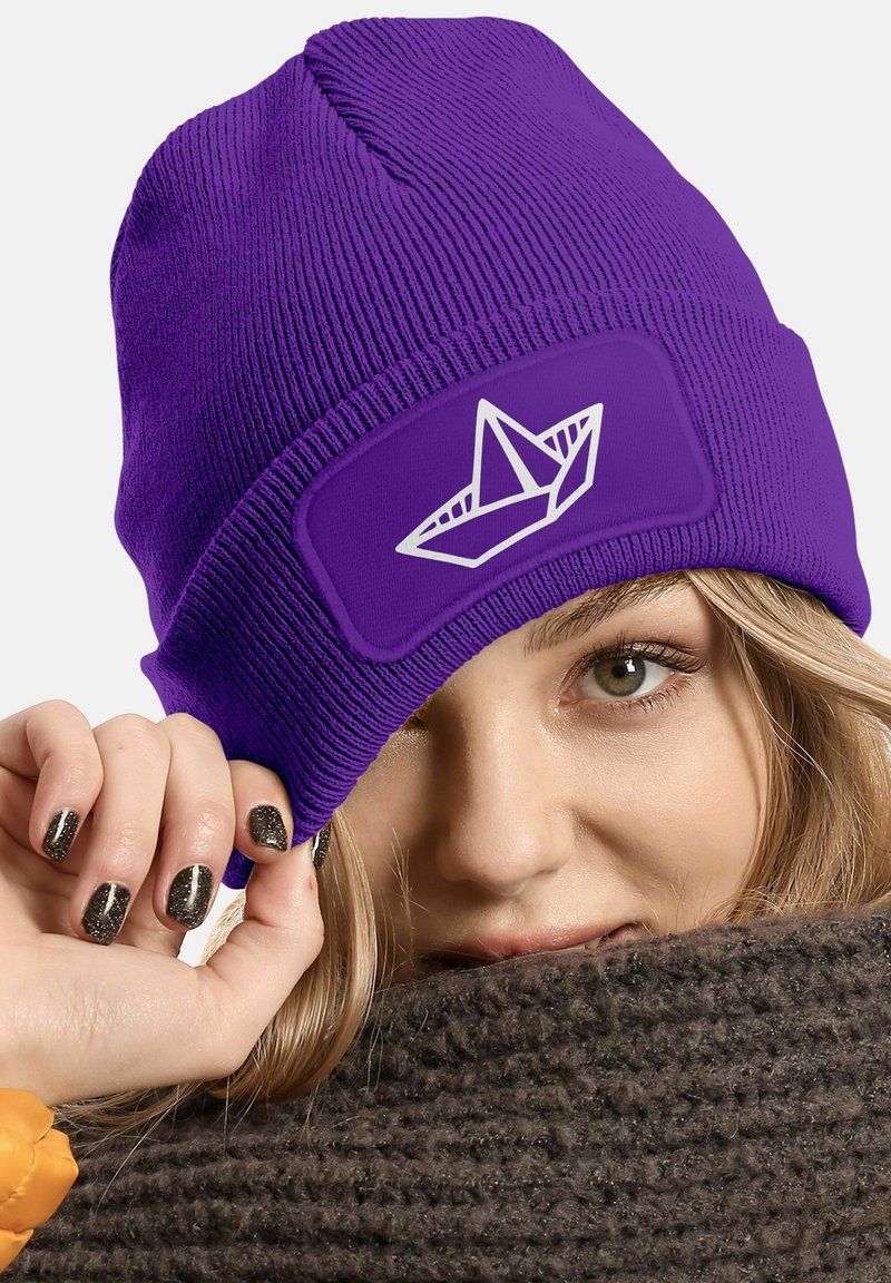 Purple knit beanie with a textured pattern and a white paper boat design on a rectangular patch. Wrapping a knitted brown scarf.