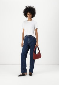 Weißes Kurzarm-T-Shirt mit kleinem Logo, hochtaillierte blaue Jeans, schwarze spitze Ballerinas und eine rote Handtasche. Glatte Stoffstrukturen.