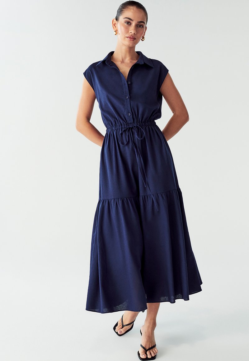 Karinė mėlyna mygtukinė suknelė su trumpomis rankovėmis, elastine juosmeniu, raišteliu ir daugiasluoksne sijonėliais. Lengvas audinys su lygiu paviršiumi.